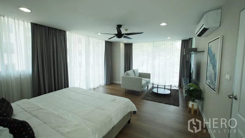 Condominium for rent in Khlong San, Bangkok - Bright corner master suite with floor-to-ceiling curtains, sofa set, and media wall.