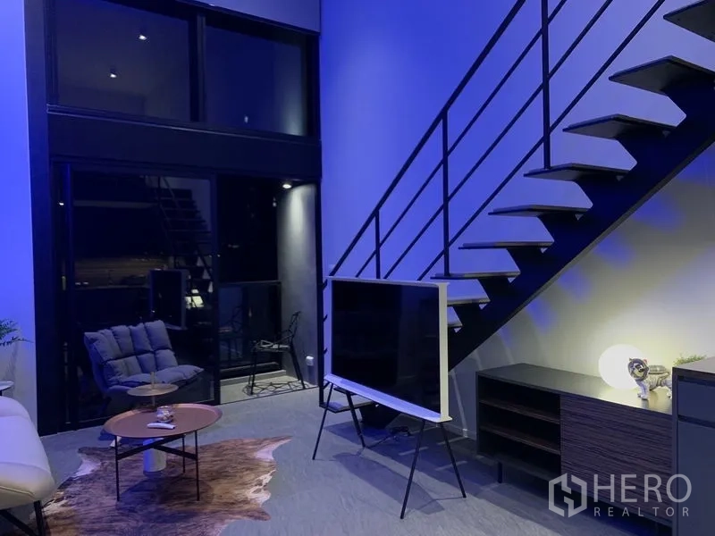 Condominium for rent in Bang Rak, Bangkok - Double-height lounge with metal staircase, floor-to-ceiling windows and TV.
