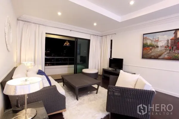 Condominium for rent in Sathon, Bangkok - Bright living room with wicker sofas, white rug, and sliding doors opening to a balcony with Bangkok skyline views at night.