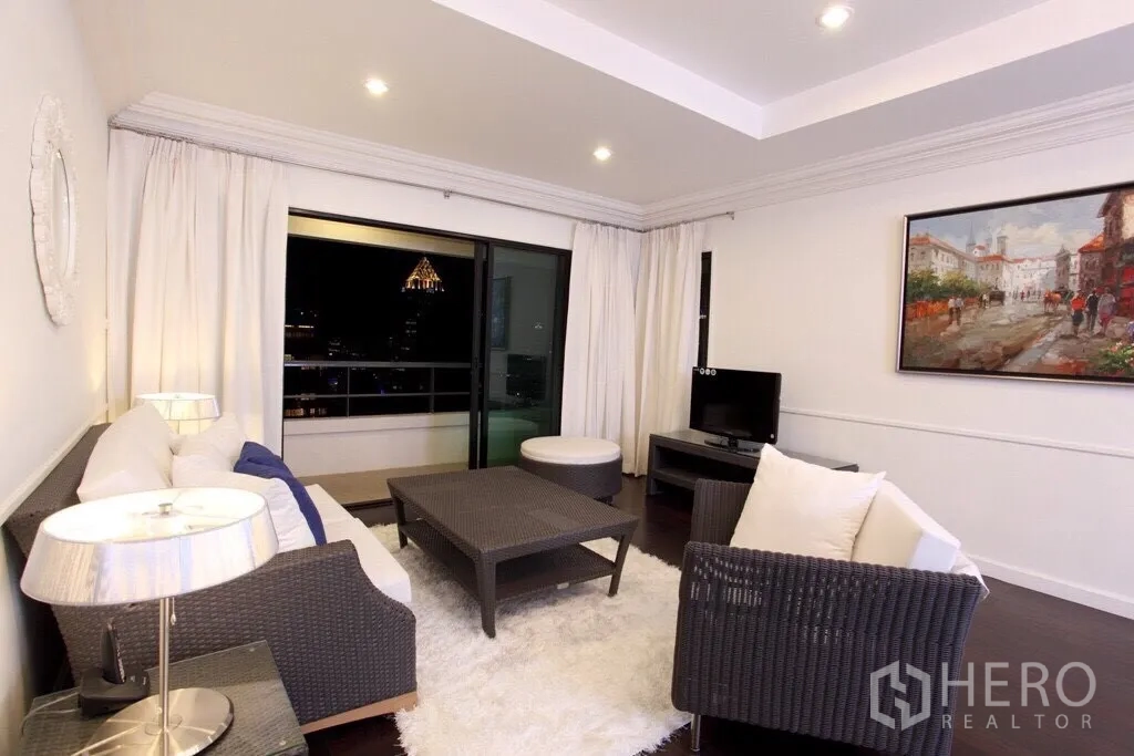 Condominium for rent in Sathon, Bangkok - Bright living room with wicker sofas, white rug, and sliding doors opening to a balcony with Bangkok skyline views at night.