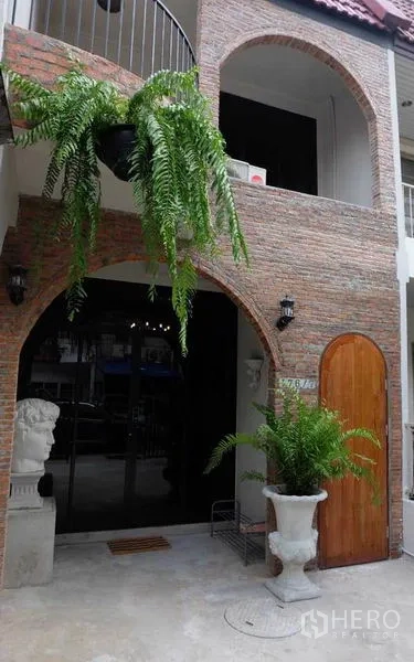 Townhouse for rent in Watthana, Bangkok - Brick-arched townhouse facade with balcony, wood door and hanging ferns.