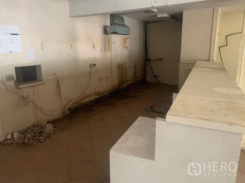 Shophouse for rent in Watthana, Bangkok - Utility zone with counter, ventilation ducting and stained wall ready for refurbishment.