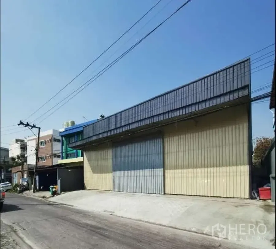 Warehouse for rent in Prawet, Bangkok - Street-facing warehouse exterior with wide sliding metal doors and a loading ramp.