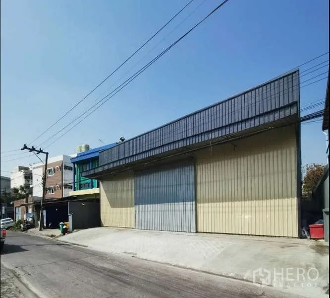 Warehouse for rent in Prawet, Bangkok - Street-facing warehouse exterior with wide sliding metal doors and a loading ramp.
