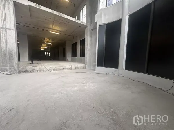 零售空间 出租在Watthana, Bangkok - 开放式一层商用空间，未完成混凝土地面与弧形玻璃立面。