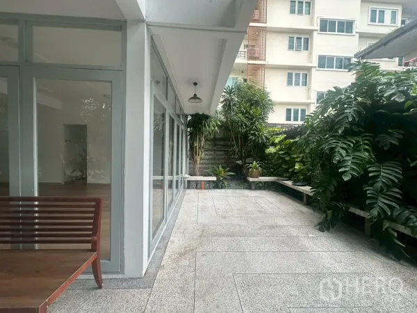 独立式住宅 出租在Watthana, Bangkok - 半室外露台，玻璃墙、长凳座位以及茂密绿植。