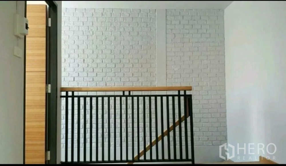 Home Office for rent in Lat Phrao, Bangkok - Second-floor landing with black metal balustrade and painted white brick feature wall.
