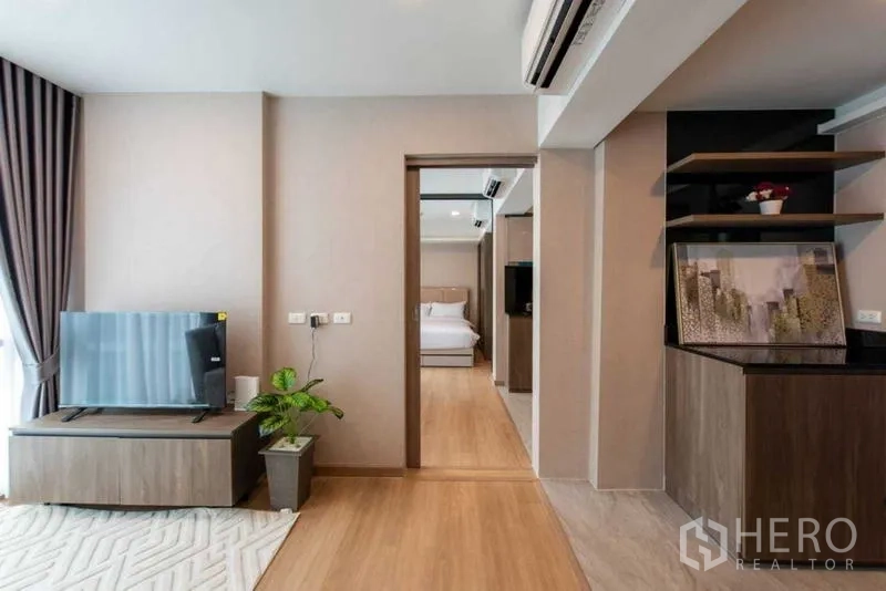 คอนโด ให้เช่าในHuai Khwang, Bangkok - ห้องนั่งเล่นคอนโดสว่างพร้อมชั้นวางทีวี พื้นไม้ และทางเข้าห้องนอน
