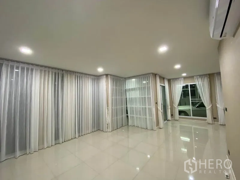 独立式住宅 出租在Prawet, Bangkok - 明亮客厅，亮面瓷砖地面、纱帘与嵌入式筒灯，空间通透。