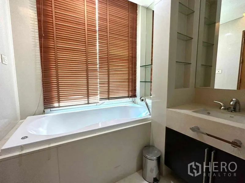 公寓 出租在Pathum Wan, Bangkok - 浴室配大尺寸浴缸，临窗木百叶，旁为单盆洗手台。