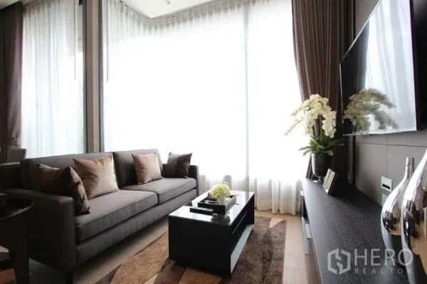 คอนโด ให้เช่าในWatthana, Bangkok - ห้องนั่งเล่นสว่างด้วยผ้าม่านโปร่ง โซฟาสีเทา โต๊ะกลาง และทีวีติดผนัง