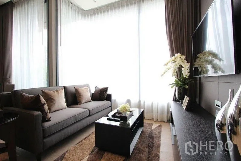 คอนโด ให้เช่าในWatthana, Bangkok - ห้องนั่งเล่นสว่างด้วยผ้าม่านโปร่ง โซฟาสีเทา โต๊ะกลาง และทีวีติดผนัง