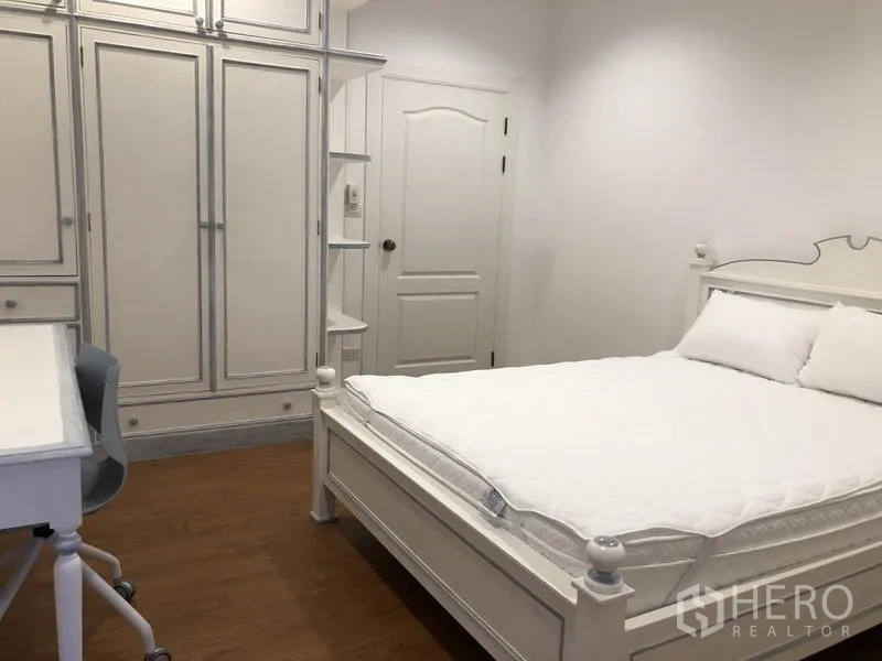 Detached House for rent in Mueang Samut Prakan, Samut Prakan - Bedroom with white bed frame, built-in wardrobes, desk and wood flooring.