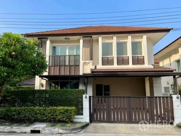 บ้าน ให้เช่าหรือขายในLat Krabang, Bangkok - ด้านหน้าบ้านเดี่ยวสองชั้น หลังคาสีน้ำตาล มีโรงจอดรถและรั้วพร้อมพุ่มไม้ตัดแต่งเรียบร้อย