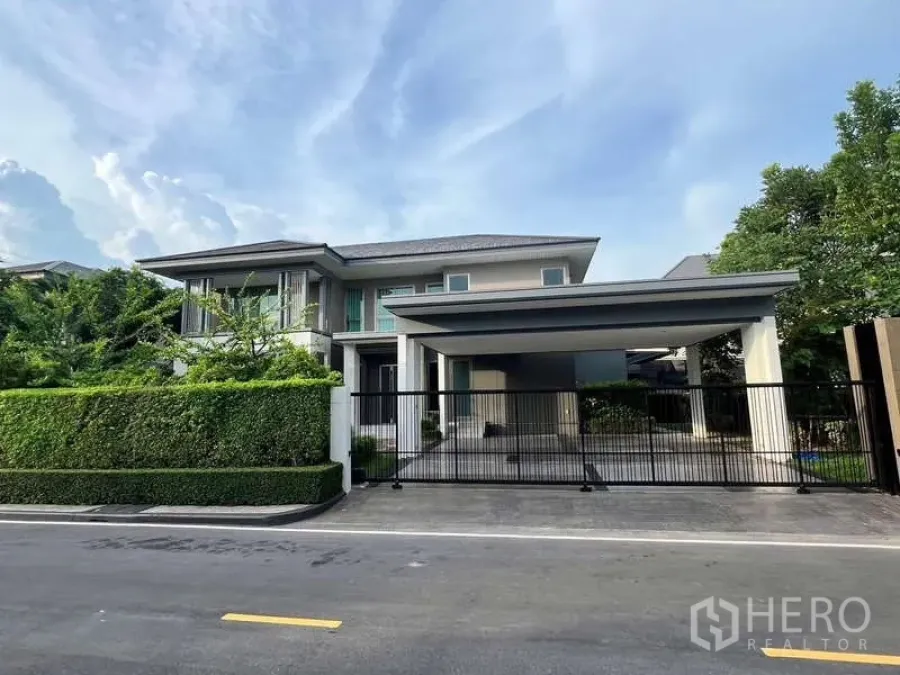 独立式住宅 出租或出售在Lat Krabang, Bangkok - 正立面带铁艺入口门，宽敞有顶车棚与修剪绿篱。