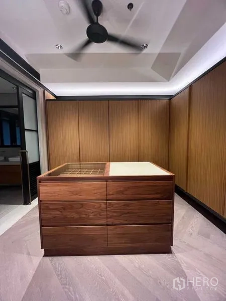 Condominium for rent in Sathon, Bangkok - Spacious walk-in closet with wood cabinetry and island drawers under a ceiling fan.