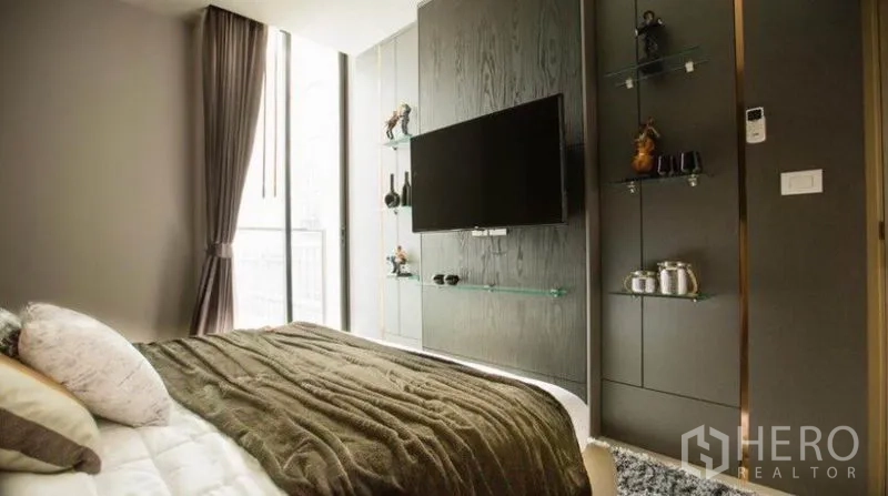 Condominium for rent in Pathum Wan, Bangkok - Second bedroom view toward TV feature wall with glass shelves and balcony light.