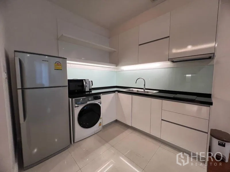 Condominium for rent in Khlong Toei, Bangkok - L-shaped kitchen with refrigerator, washer-dryer, microwave and under-cabinet lighting.