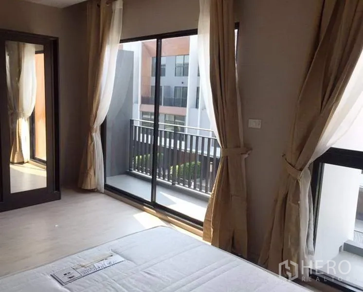 Townhouse for rent in Suan Luang, Bangkok - Bedroom with large sliding glass doors to a private balcony, full curtains and mirrored wardrobe.