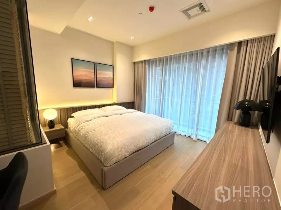Condominium for rent in Bangkok - Cozy Thonglor condo bedroom with king bed, warm bedside lighting, wall art, and sheer floor-to-ceiling curtains.