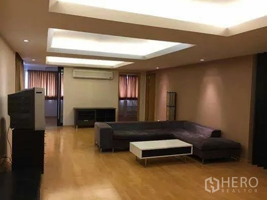 公寓 出租在Watthana, Bangkok - 宽敞客厅，L形沙发、嵌灯吊顶与木地板，配有电视柜。