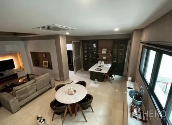 Townhouse for rent in Yan Nawa, Bangkok - Open-plan living and dining area with sofa, round table, and wall cabinets beside large windows.