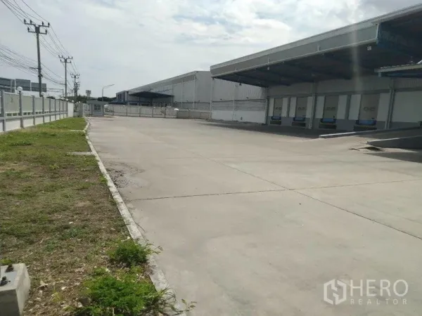 Warehouse for rent in Samut Prakan - Wide truck yard with covered loading docks and dock levelers along the warehouse exterior.