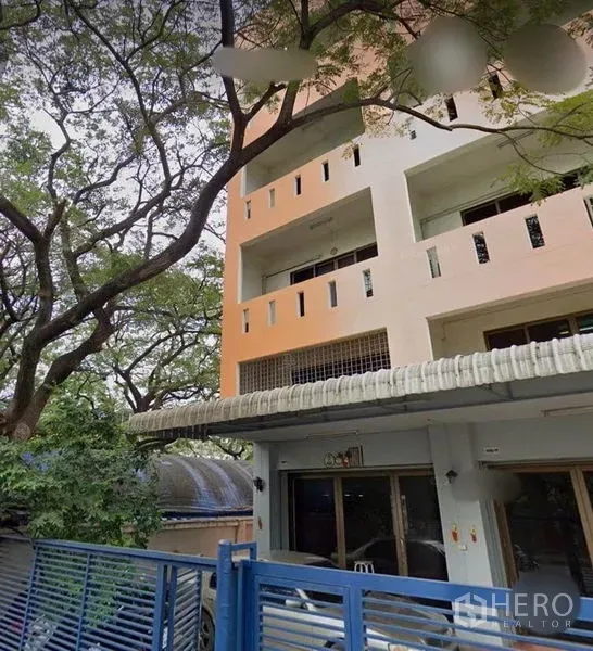 联排别墅 出售在Wang Thonglang, Bangkok - 四层联排别墅外观，带开放式阳台和蓝色金属大门，门前有大树，位于曼谷旺通朗区。