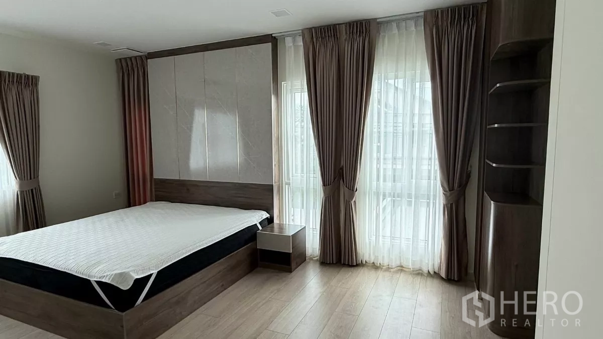 Detached House for rent in Bang Phli, Samut Prakan - Master bedroom corner with large windows, sheer curtains, and a bedside table.