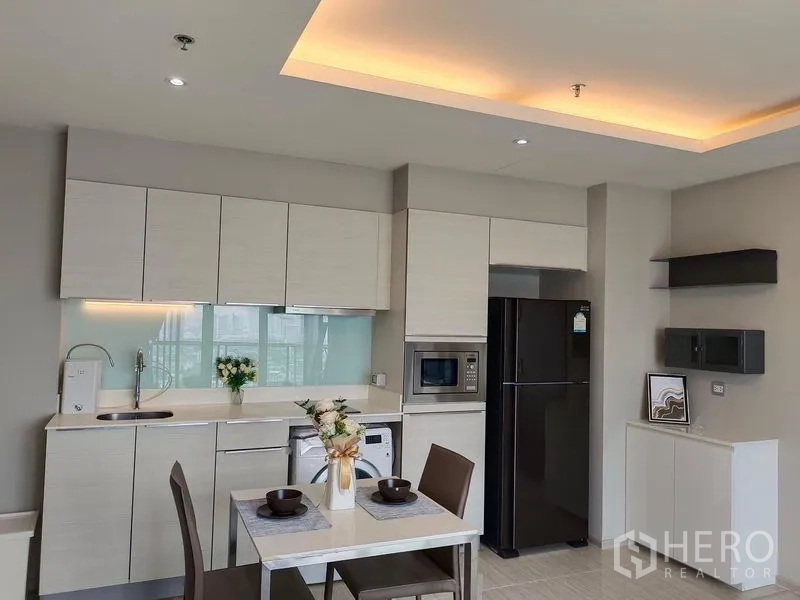 Condominium for rent in Watthana, Bangkok - Light-tone kitchen with ample cabinets, fridge, microwave and a two-seat dining table.