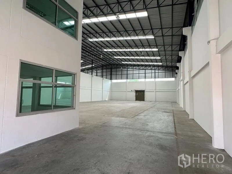 Warehouse for rent in Mueang Samut Prakan, Samut Prakan - Interior view of warehouse with adjacent windowed office block and high roof.