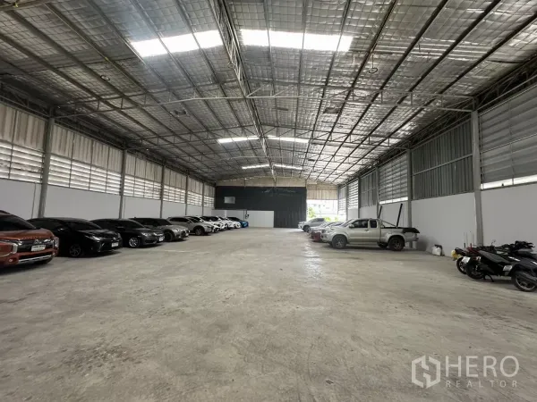 Warehouse for rent in Suan Luang, Bangkok - High-ceiling warehouse interior with insulated metal roof, skylights, concrete floor, and vehicles lined along the walls.