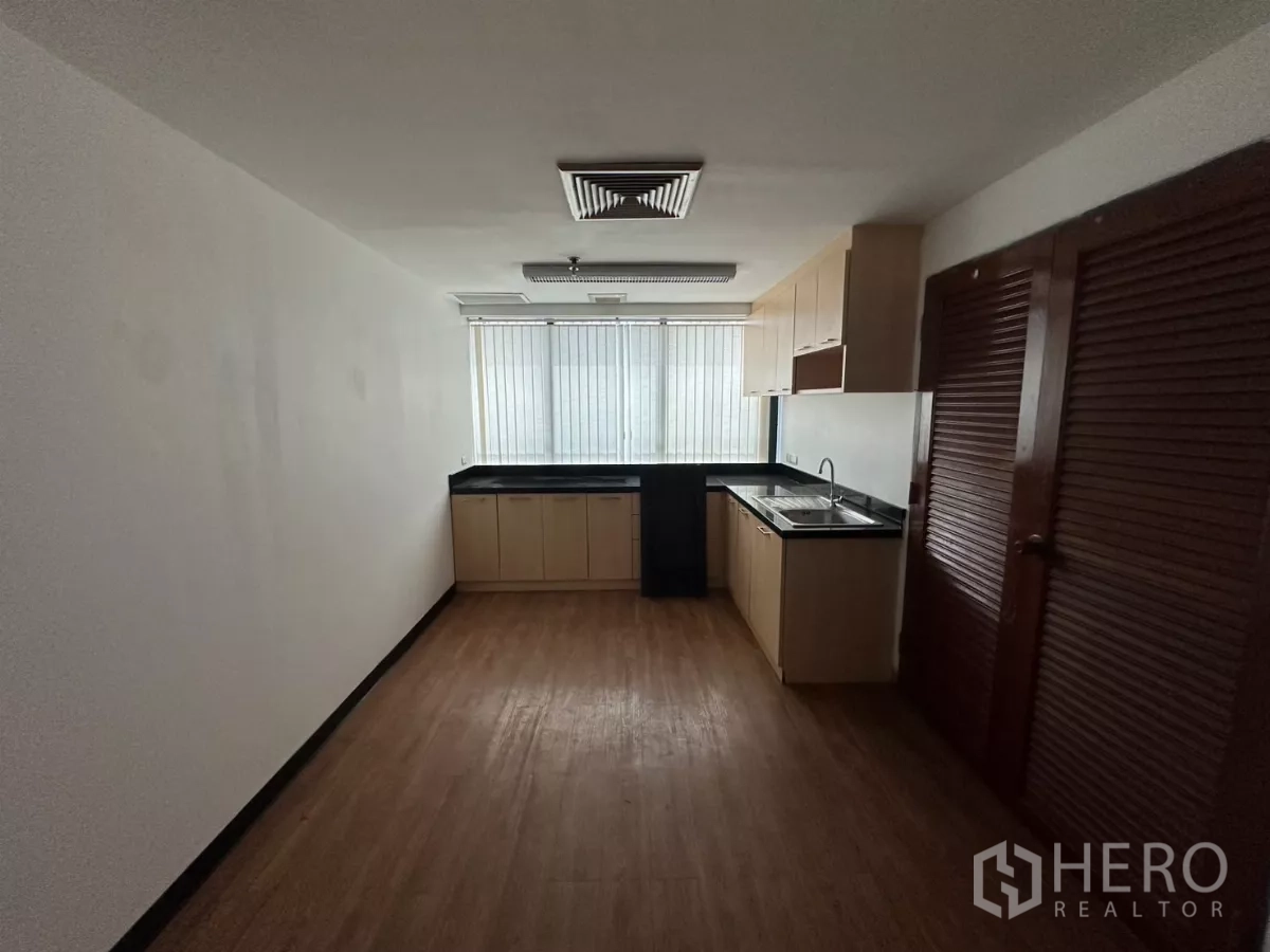 Office Space for rent in Watthana, Bangkok - Pantry with built-in cabinets, sink and black countertops beside window blinds.