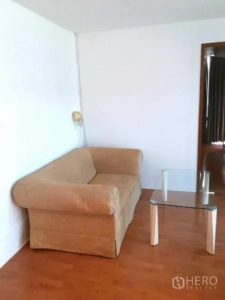 Condominium for rent in Watthana, Bangkok - Compact living corner with beige loveseat and a glass coffee table on warm wood flooring.