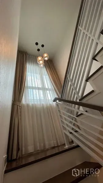 Detached House for rent in Bang Kapi, Bangkok - Bright stairwell with tall window, sheer curtains, pendant lights and white railing.