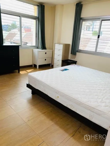 Townhouse for rent or sale in Huai Khwang, Bangkok - Master bedroom with large windows, light wood floors and a queen bed with dressers