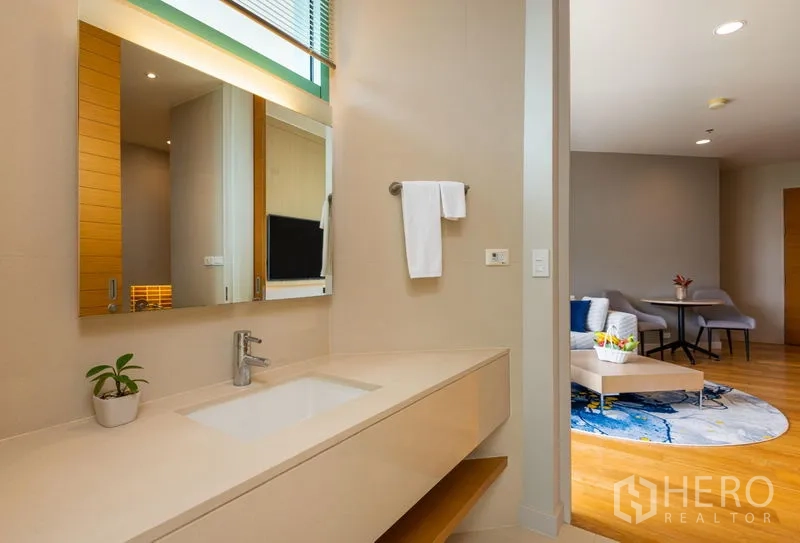 Condominium for rent in Bang Kho Laem, Bangkok - Minimalist vanity counter with mirror and towel rail opening to a living room with seating and coffee table.