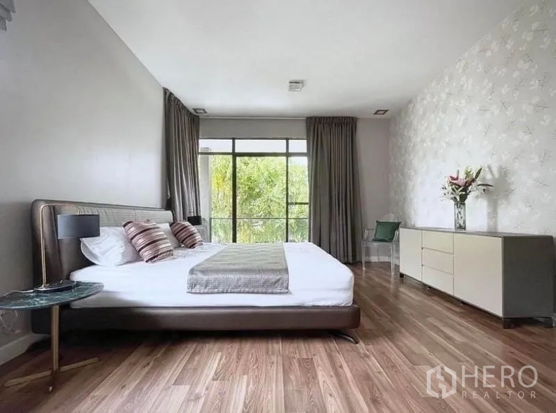 Detached House for rent in Prawet, Bangkok - Spacious bedroom with wood flooring, dresser, bedside tables and full‑height windows.