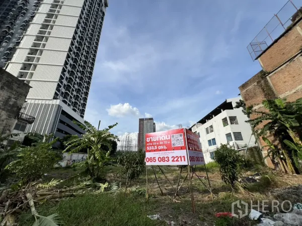 Land for sale in Suan Luang, Bangkok - Vacant urban land with a sale sign, bordered by high‑rise and low‑rise buildings under a blue sky.
