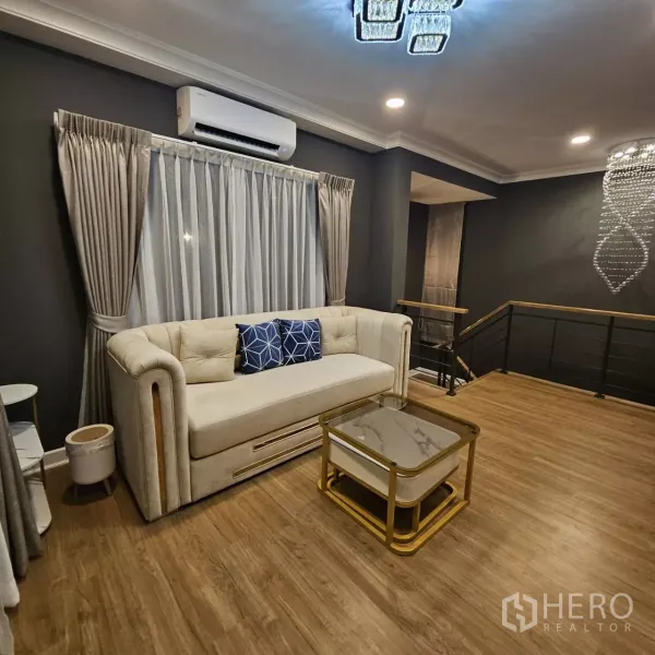 独立式住宅 出租在Bang Phli, Samut Prakan - 二层家庭起居区，沙发与茶几、木地板、深色点缀墙和空调。