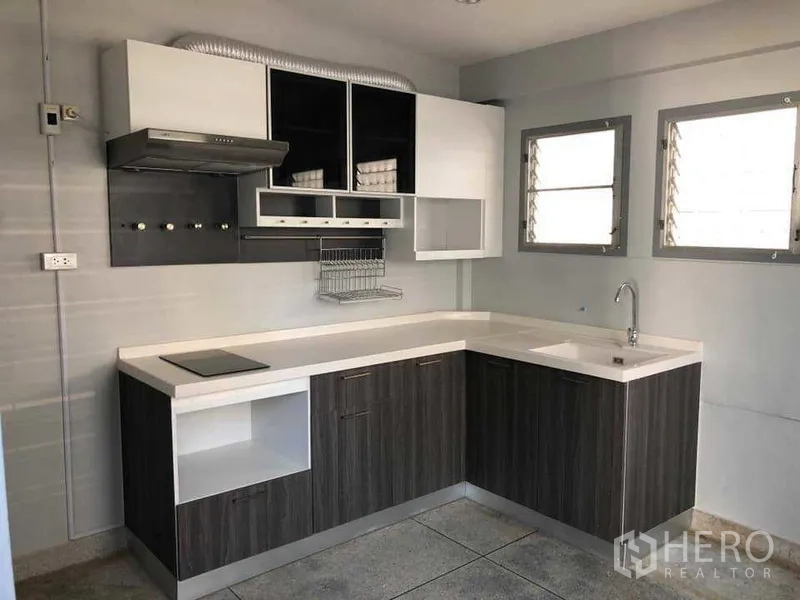 Detached House for rent in Phra Khanong, Bangkok - Renovated L‑shaped kitchen with white countertops, hob, range hood and storage.