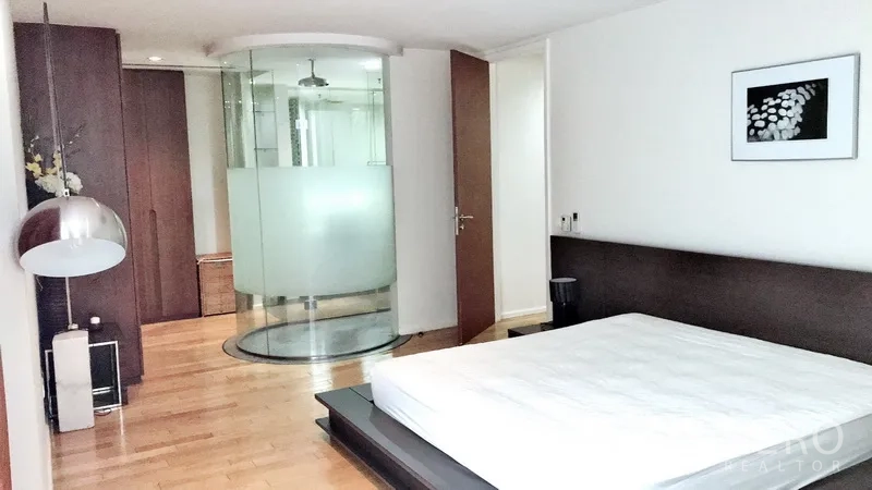 Condominium for rent in Bang Rak, Bangkok - Master bedroom with platform bed, built-in wardrobes and a curved glass shower enclosure.