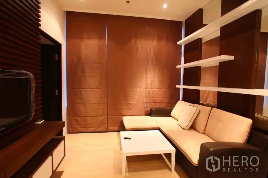 公寓 出租在Watthana, Bangkok - 曼谷瓦塔那区公寓客厅，L 型沙发、墙面搁架、茶几与遮光窗帘，氛围温馨。