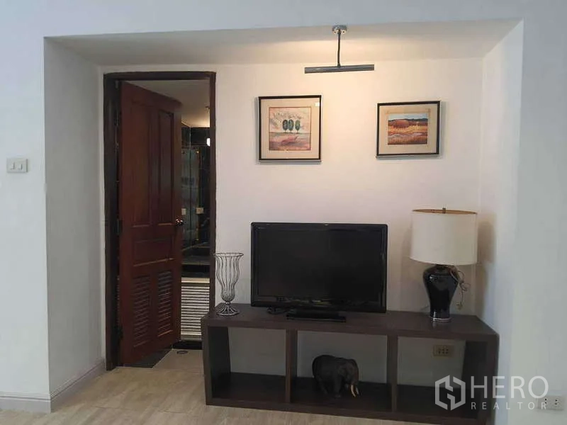 Townhouse for rent in Khlong Toei, Bangkok - TV nook with framed art and wooden door to bathroom.