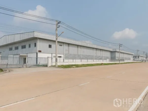 工厂 出租在Si Racha, Chon Buri - 宽阔工业道路旁的浅灰色金属厂房外观，带围栏与电线杆