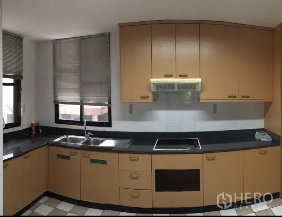 Condominium for rent in Watthana, Bangkok - L-shaped kitchen with black countertops, double sink, electric cooktop, exhaust hood and two windows with blinds.