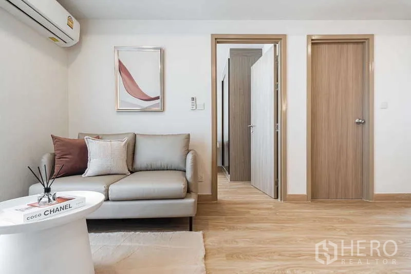 Condominium for rent - Cozy living room with neutral sofa, wall art, and doors leading to bedroom and bathroom.