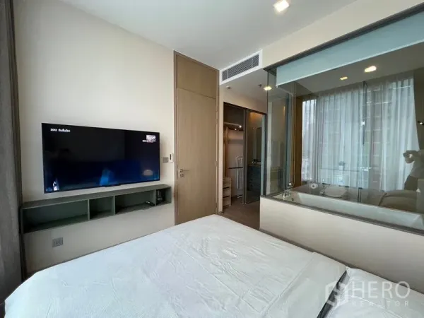 公寓 出租在Watthana, Bangkok - 卧室配壁挂电视，玻璃隔断可见带浴缸的卫浴间。
