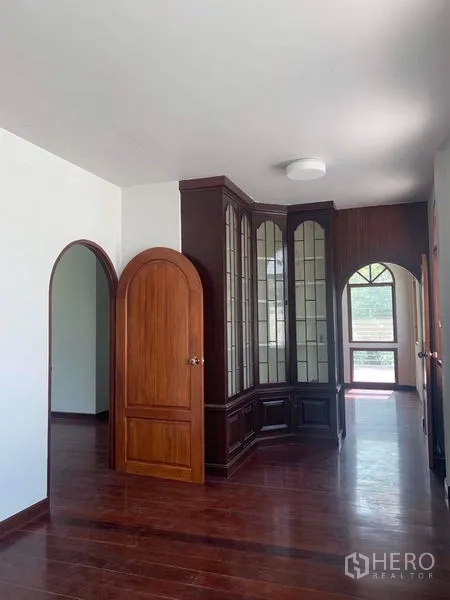 独立式住宅 出租在Ratchathewi, Bangkok - 走廊设拱形木门与落地玻璃展示柜，深色木地板。