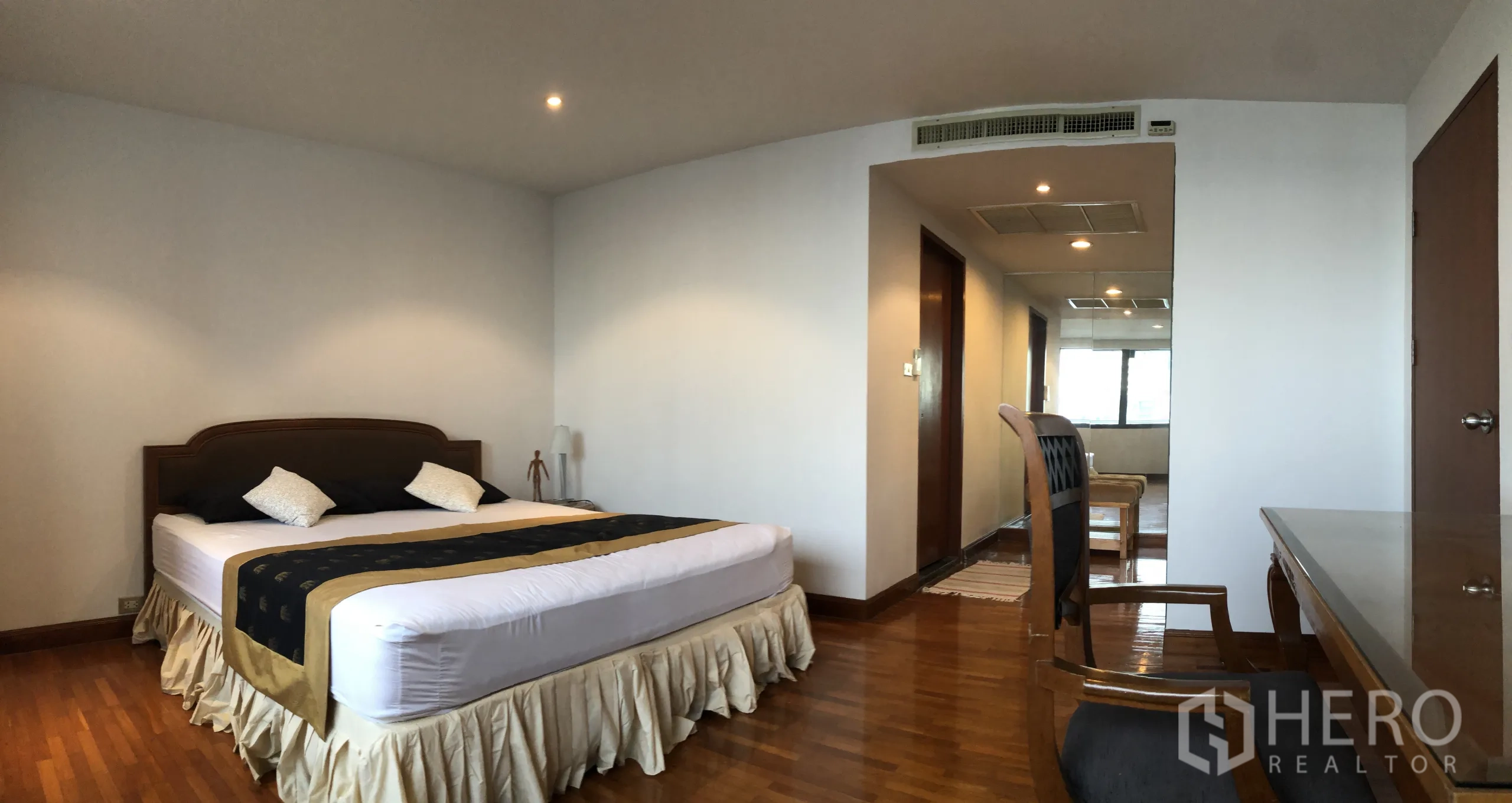 Condominium for rent in Khlong Toei, Bangkok - Bedroom angle showing bed, study desk and hallway to bathroom on warm wood floors.